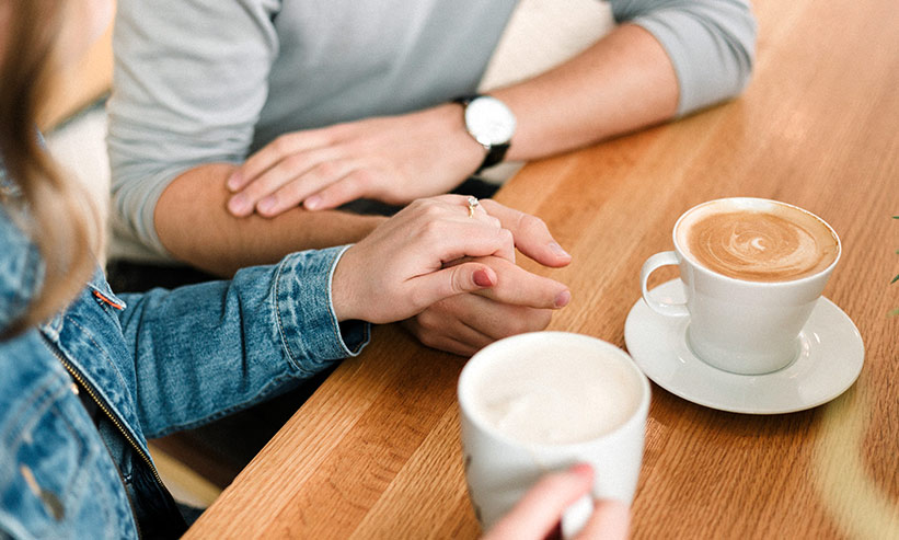 カフェでコーヒーを飲みながら手を握るカップル