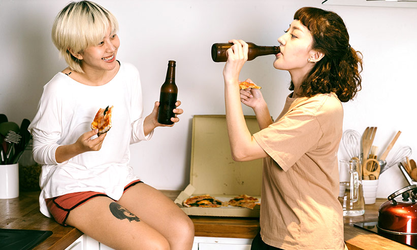 ピザを食べながらビールを飲む2人の女性