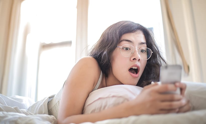 ベッドでスマートフォンを見る女性