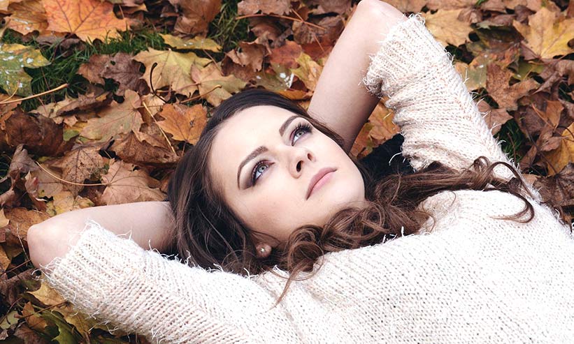 枯れ葉の上に仰向けに寝転ぶ女性