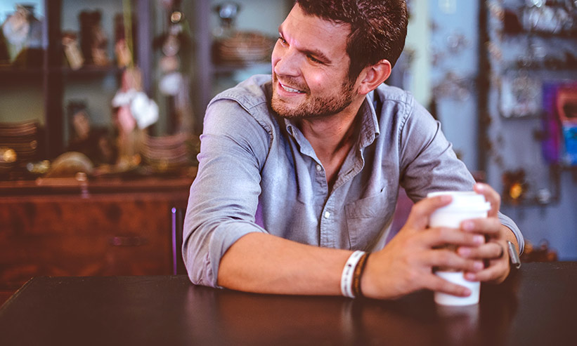 カフェでコーヒーを持ち微笑む男性